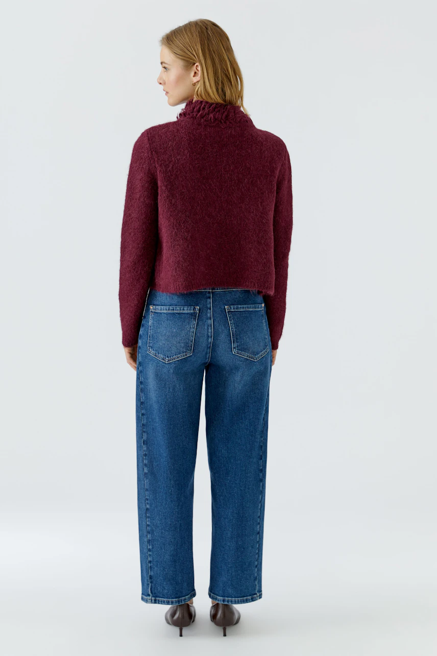 Woman in a cozy burgundy cardigan, paired with blue jeans, viewed from the back.