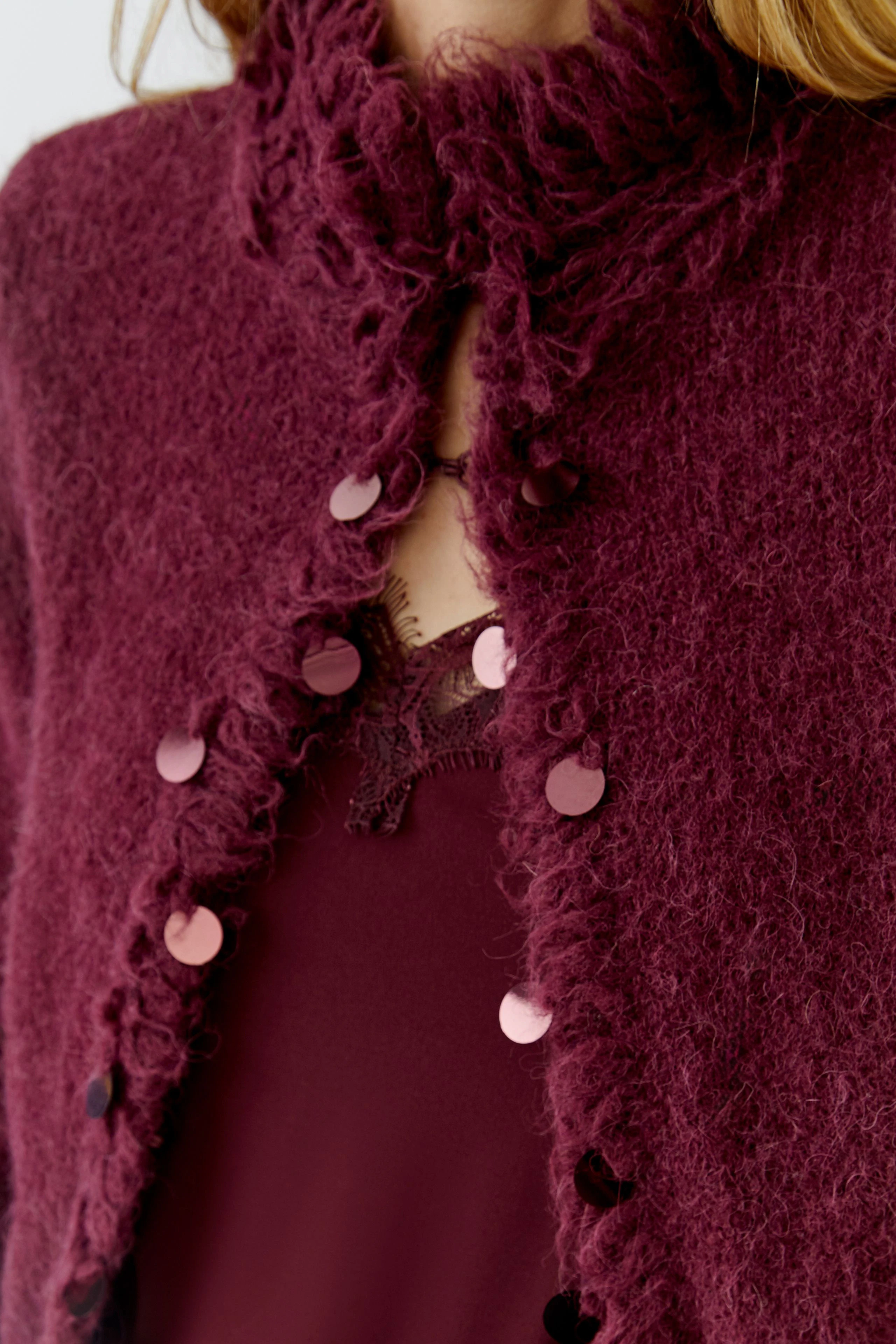 Woman in a textured burgundy cardigan with decorative buttons, wearing a matching lace top.