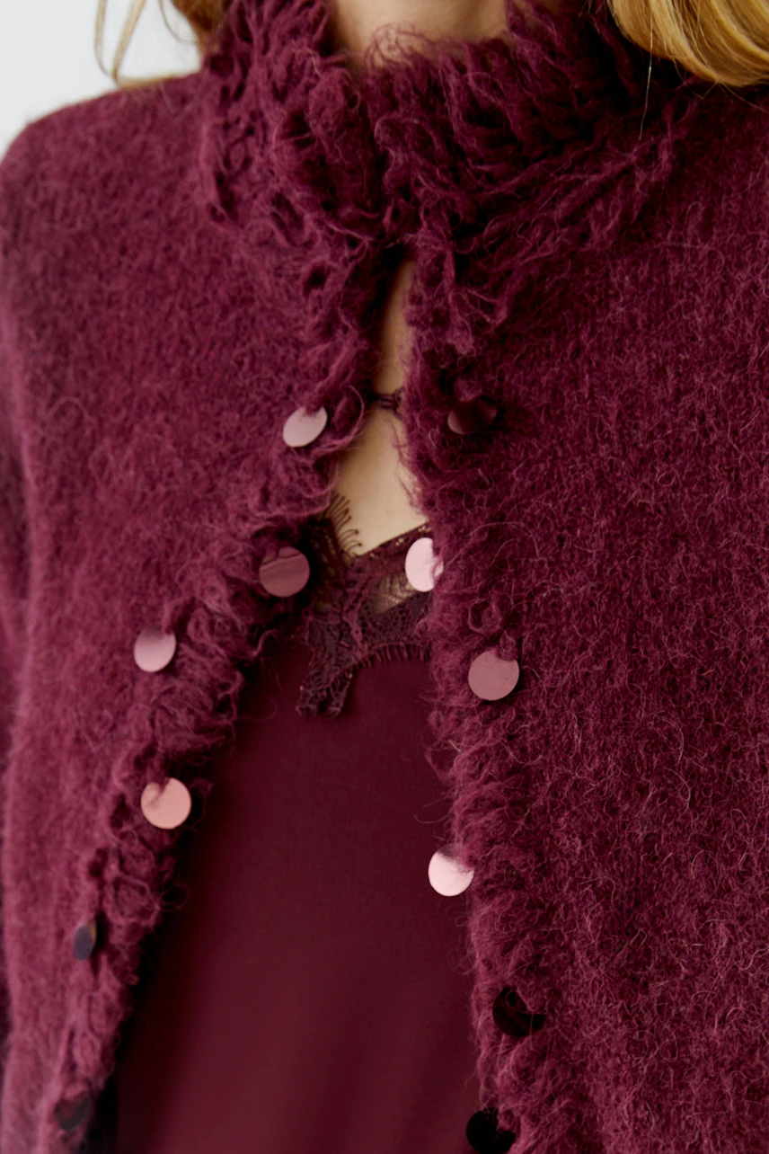 Woman in a textured burgundy cardigan with decorative buttons, wearing a matching lace top.