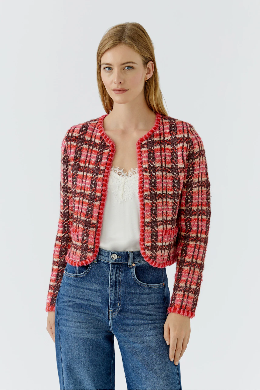 Frau in karierter Strickjacke: Rote und schwarze Muster, kombiniert mit weißem Top und blauer Jeans.
