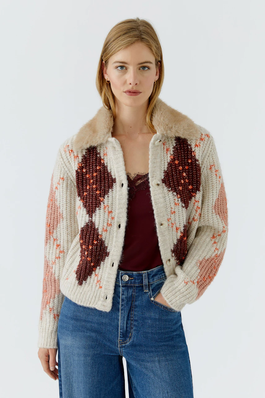Strickjacke: Frau in gemusterter Strickjacke mit Fellkragen, kombiniert mit Jeans und Top.