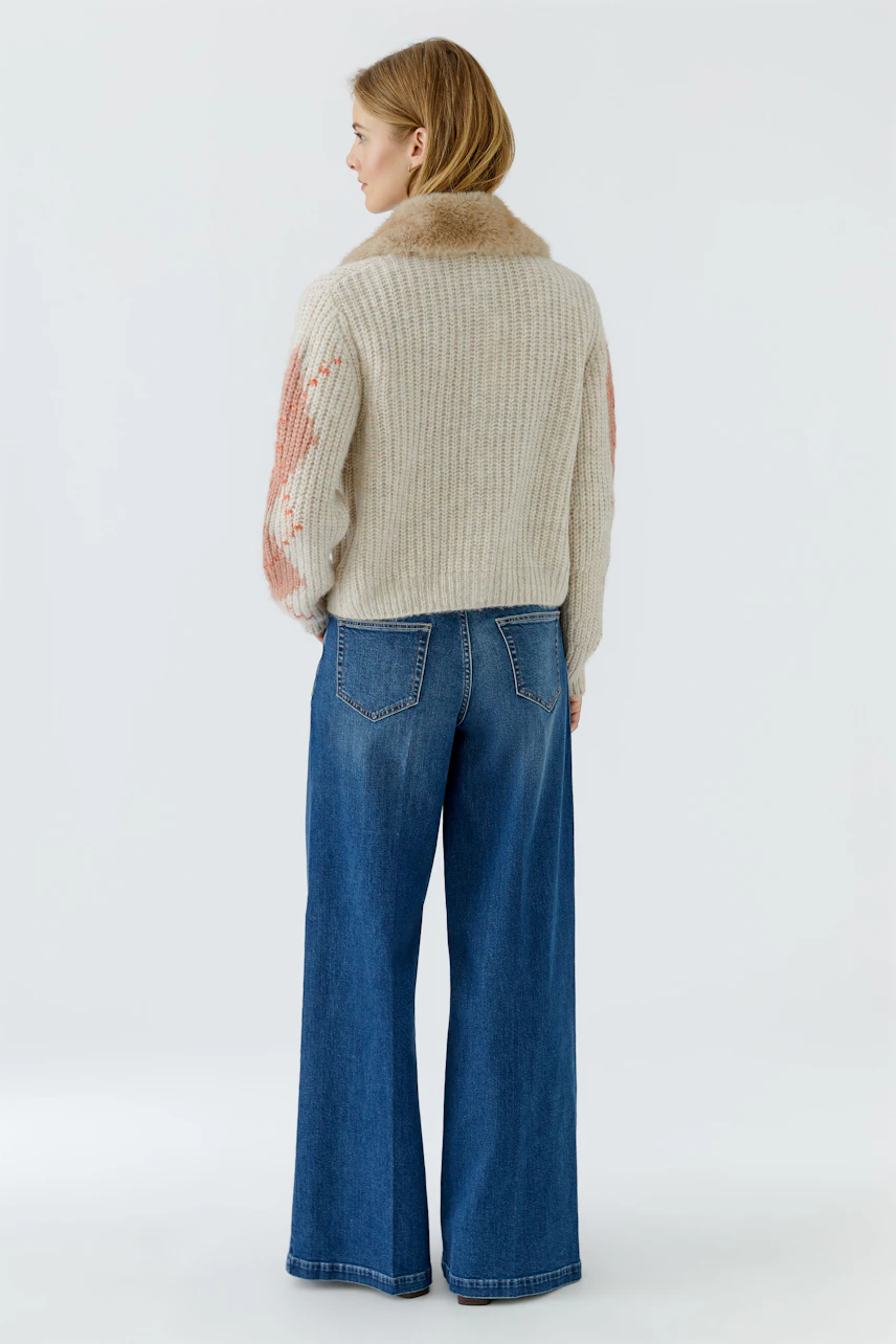 Strickjacke: Frau in beiger Strickjacke mit Muster, kombiniert mit blauer Jeans, von hinten zu sehen.