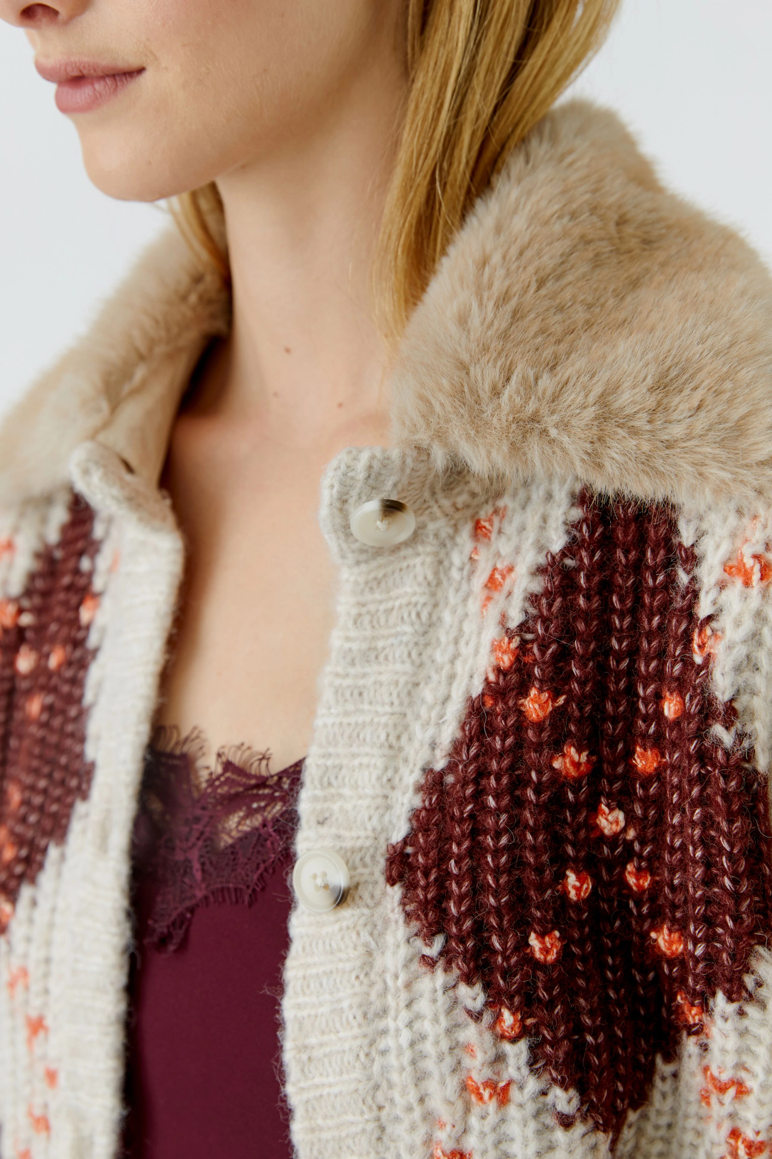 Strickjacke: Frau in gemusterter Strickjacke mit Fellkragen und rotem Top darunter.