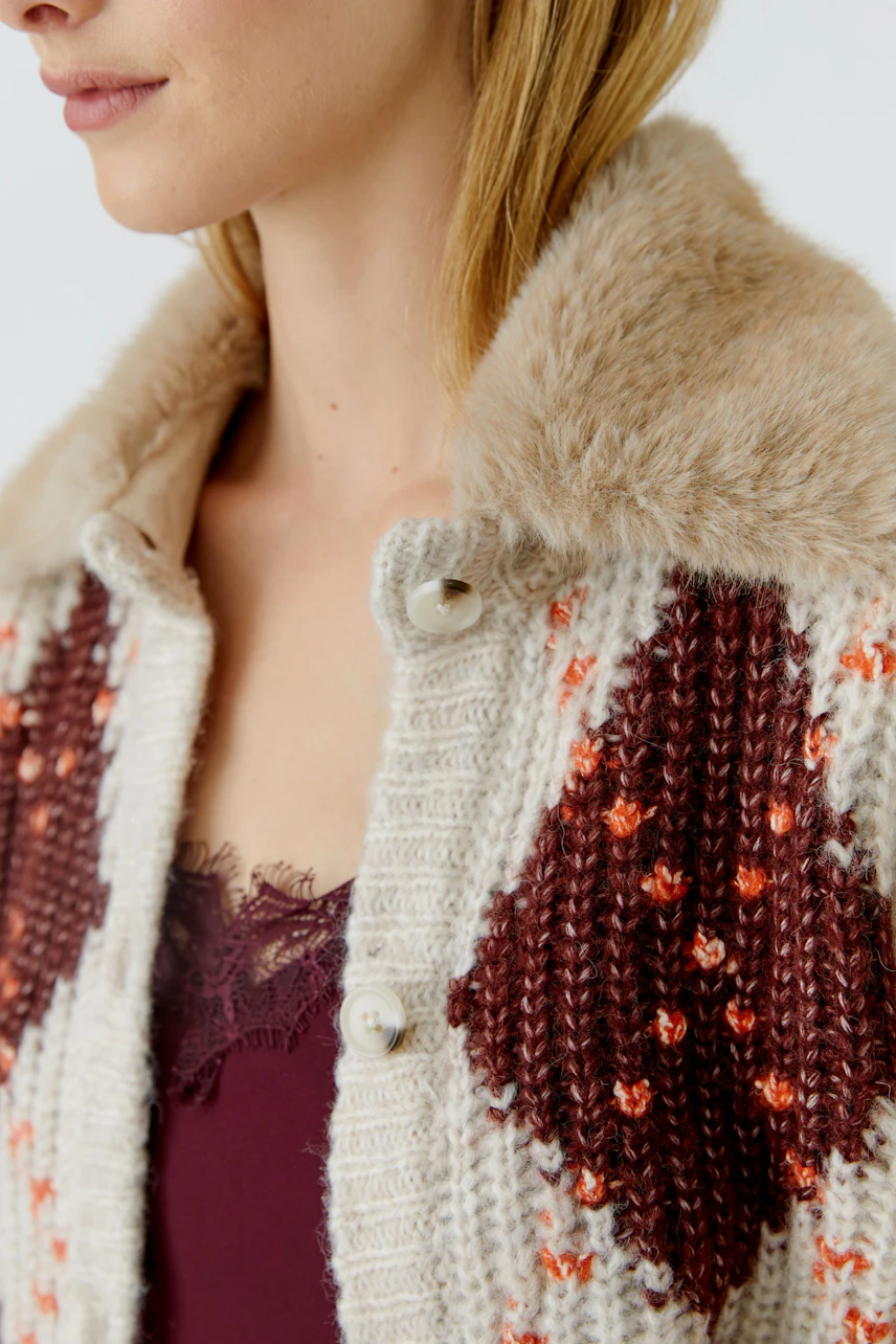 Strickjacke: Frau in gemusterter Strickjacke mit Fellkragen und rotem Top darunter.