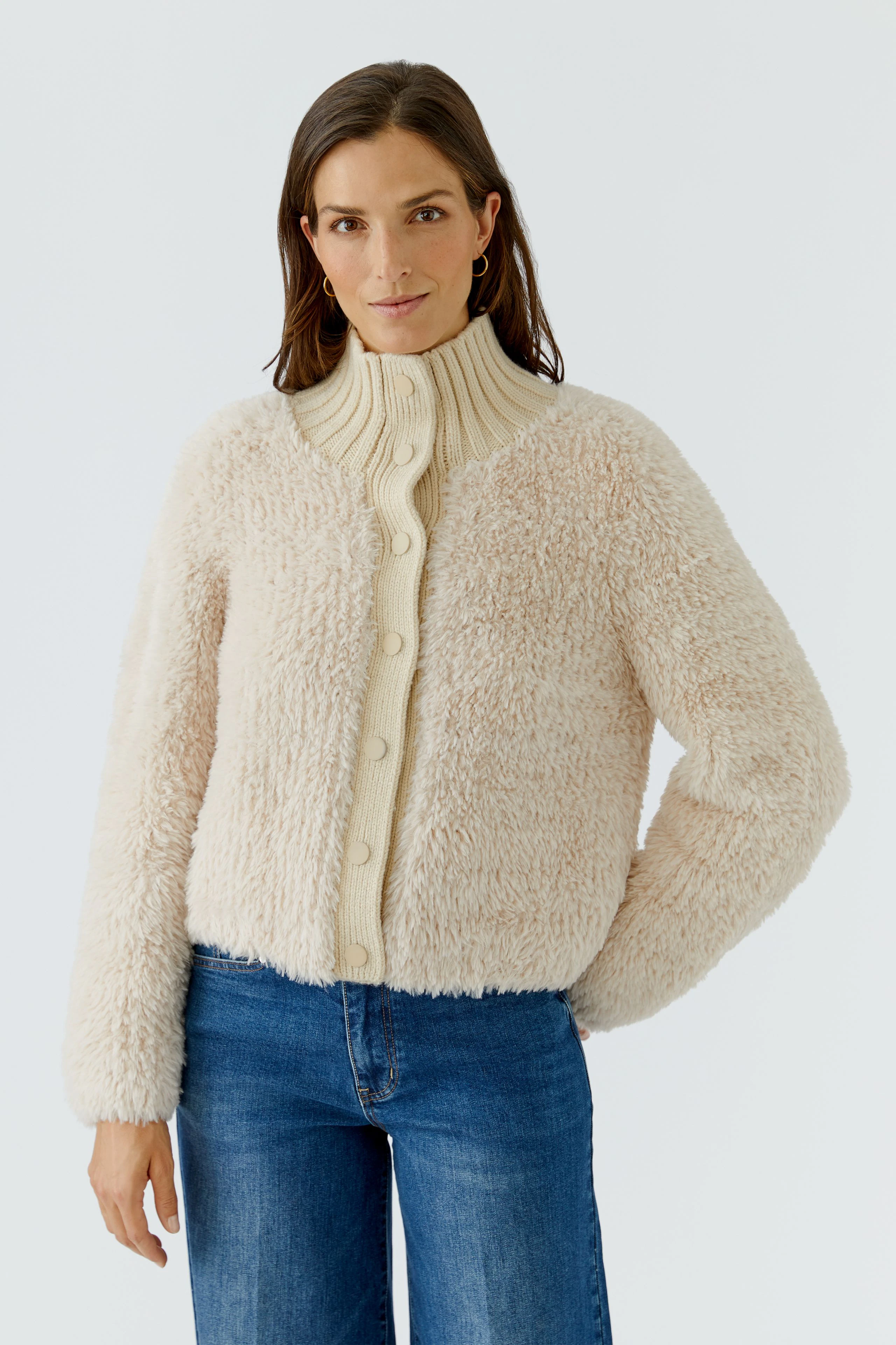 Frau in flauschiger Strickjacke mit Knopfleiste, kombiniert mit blauer Jeans, schaut freundlich.