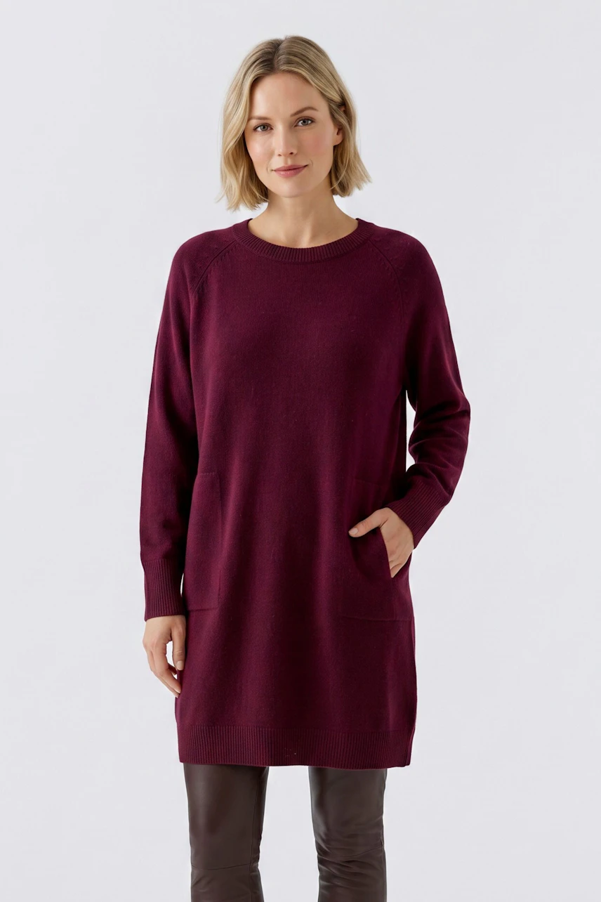 Strickkleid: Frau im weinroten Strickkleid mit Taschen, kombiniert mit braunen Lederleggings.