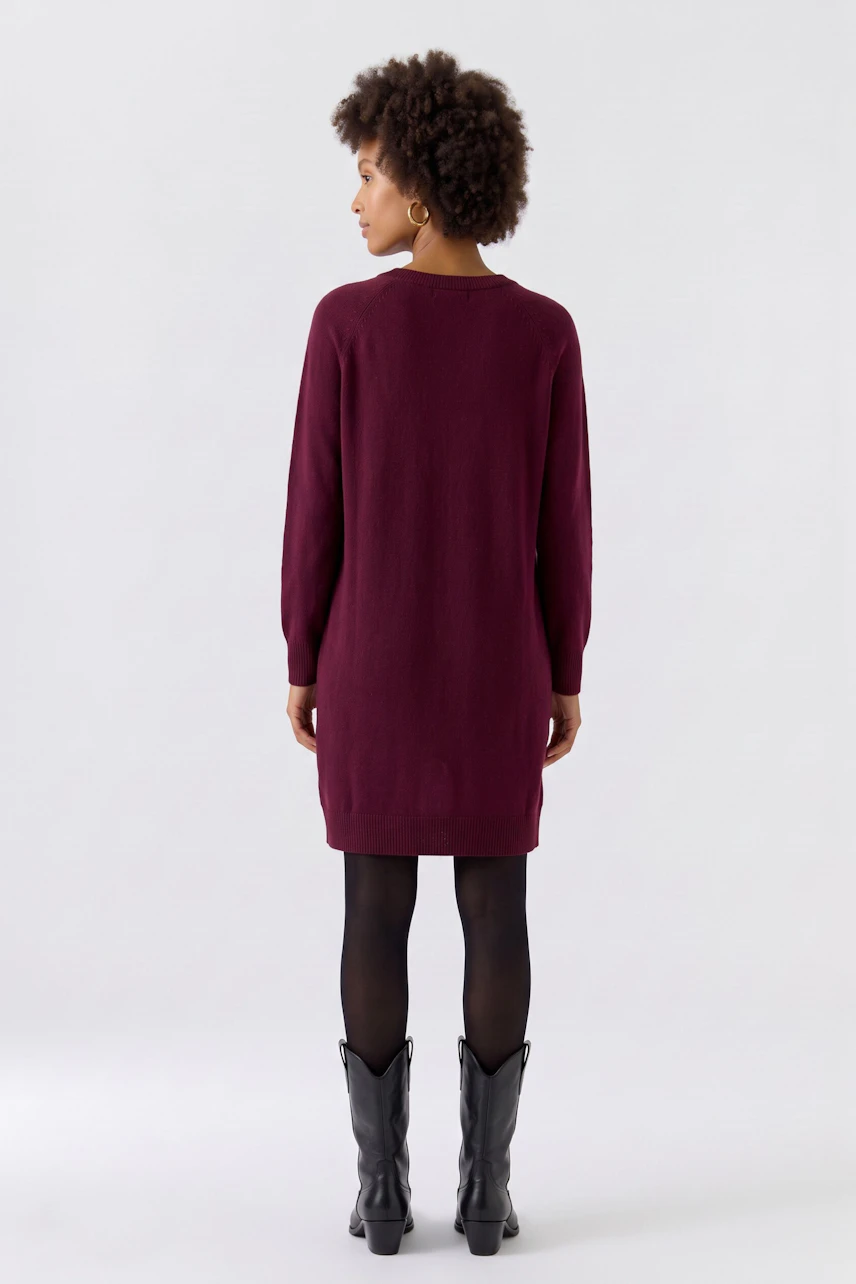 Casual knit dress: Woman in a burgundy knit dress paired with brown leather leggings, looking relaxed.