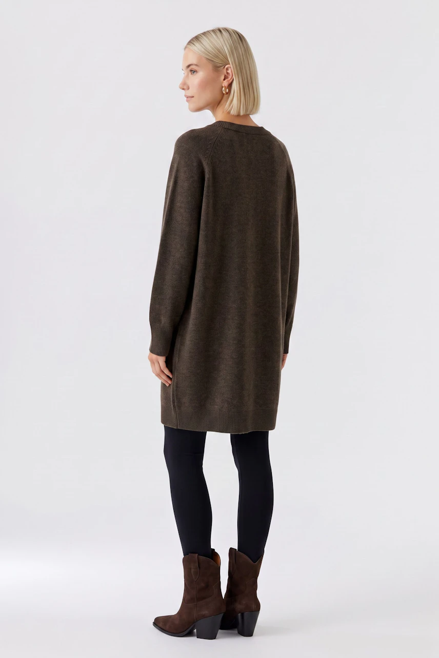 Strickkleid: Frau im braunen Strickkleid, schwarze Leggings und braune Stiefel, seitlich stehend.