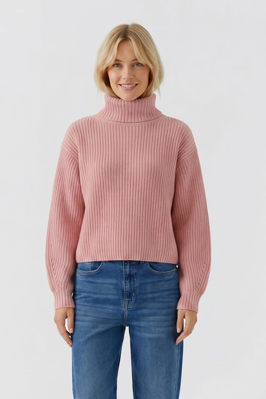Frau im rosa Pullover mit Rollkragen, kombiniert mit blauer Jeans, lächelt freundlich.