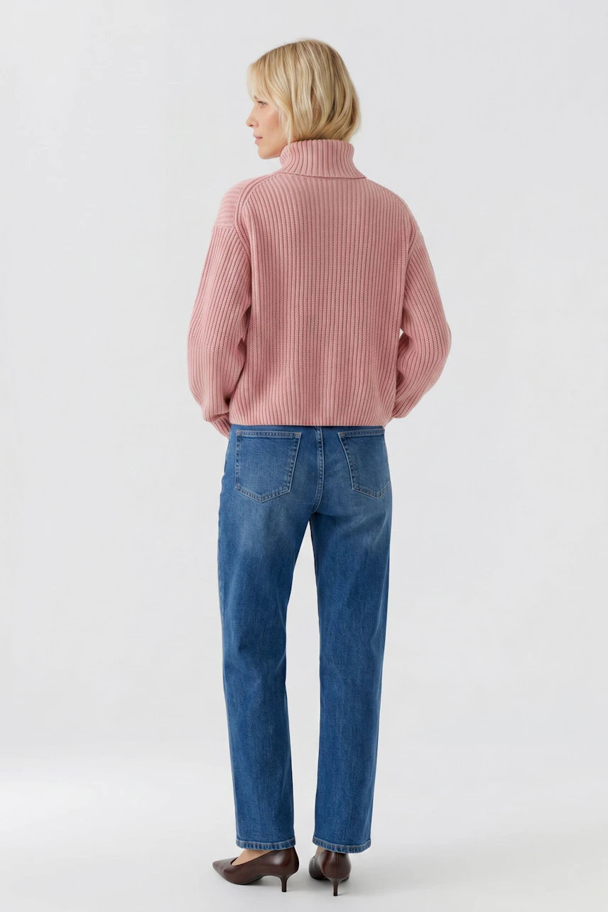 Frau im rosa Pullover mit Rollkragen, kombiniert mit blauer Jeans, von hinten gesehen.