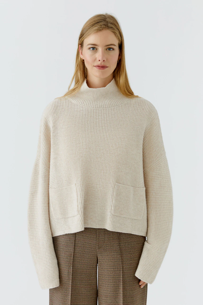 Damen-Pullover: Frau im beigen Strickpullover mit Taschen, kombiniert mit brauner Hose, lächelt dezent.