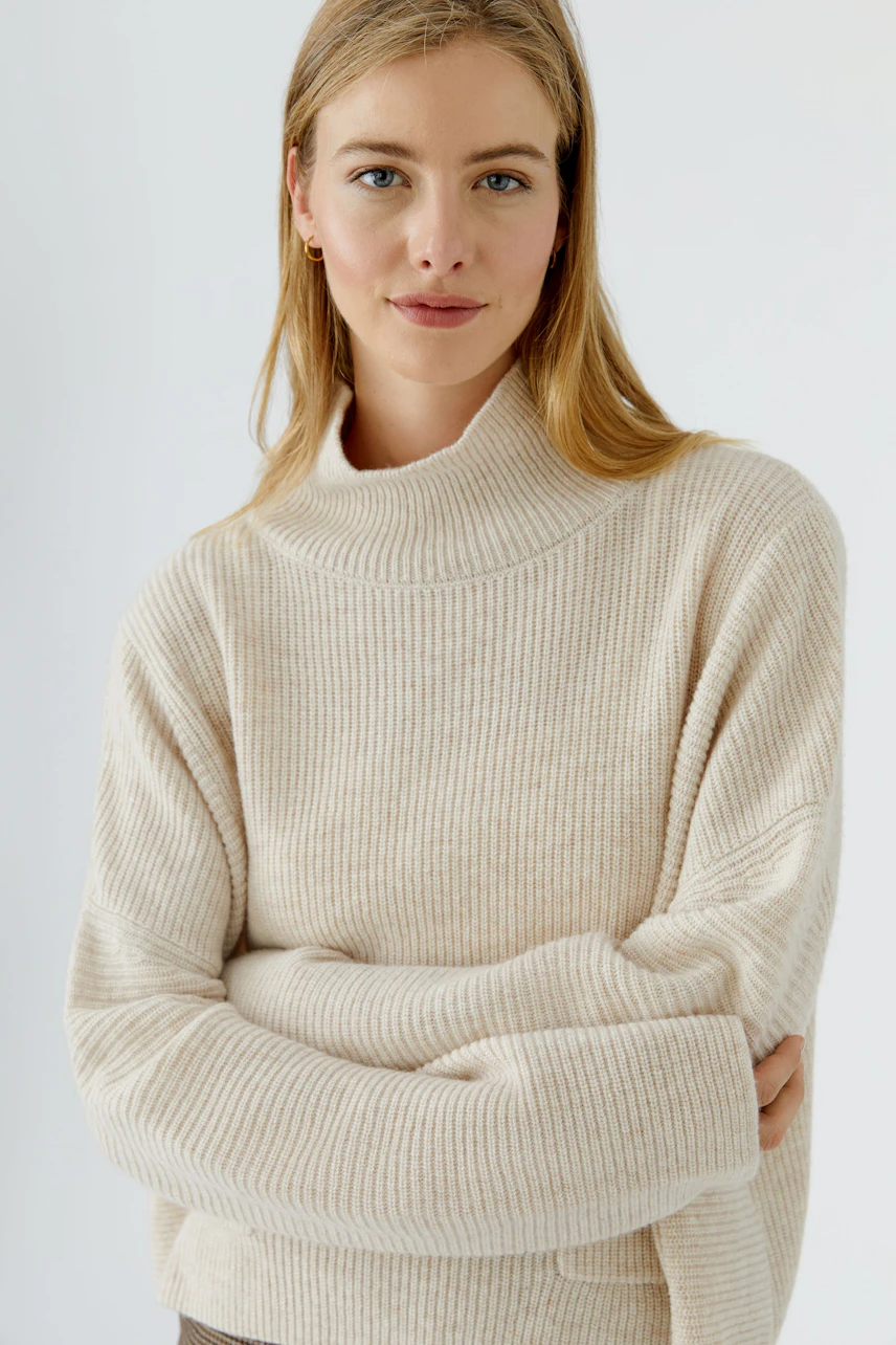 Frau im beigen Pullover: Lässiger Strickpullover mit hohem Kragen, ideal für kühle Tage.