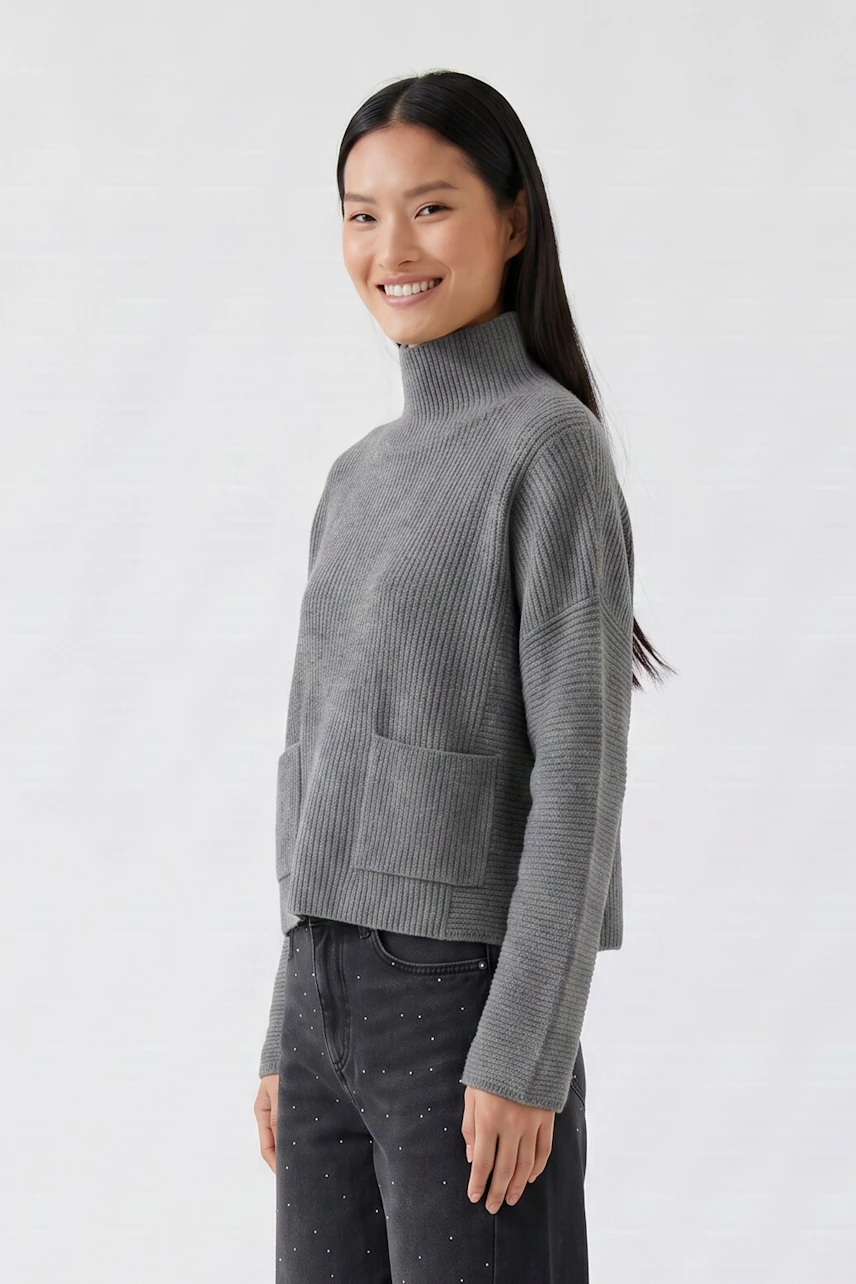 Grauer Damen-Pullover: Frau im gerippten Pullover mit Stehkragen und Taschen, kombiniert mit dunkler Jeans.