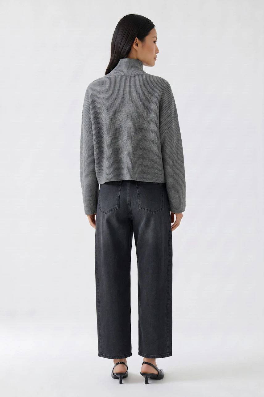 Grauer Damen-Pullover: Frau im lockeren Pullover mit Stehkragen und dunkler Jeans von hinten.