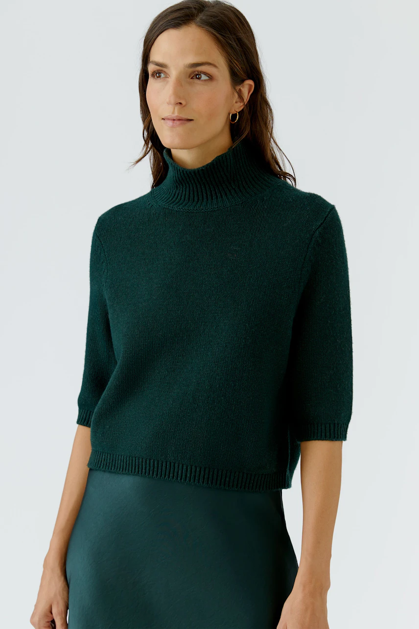 Casual women's pullover: Woman in a green turtleneck pullover with short sleeves, paired with a matching skirt.