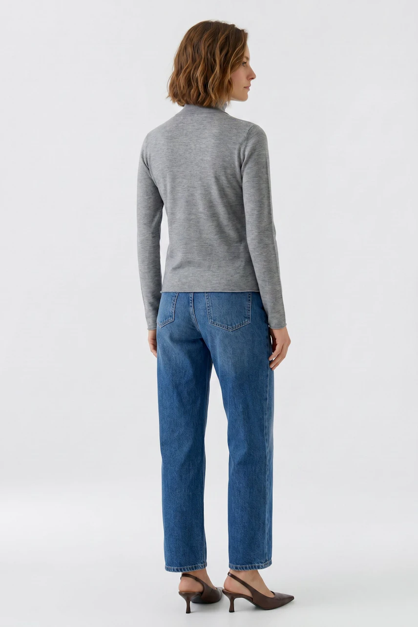 Casual women's pullover: Woman in a gray pullover and blue jeans, viewed from the back.