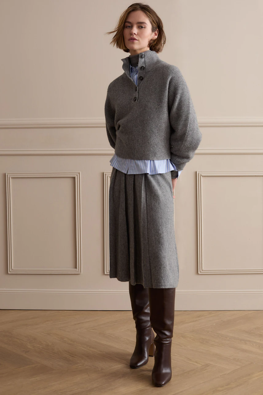Casual women's pullover: Woman in a grey pullover over a blue shirt, paired with a matching skirt and boots.