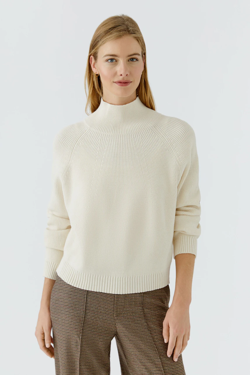 Casual women's pullover: Woman in a cream pullover with a high neck and relaxed fit, paired with checkered pants.