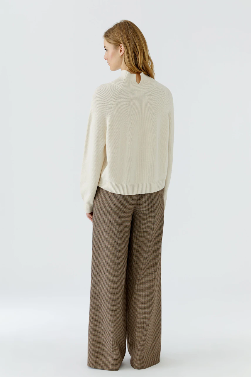 Casual women's pullover: Woman in a cream pullover and wide brown trousers, viewed from the back.