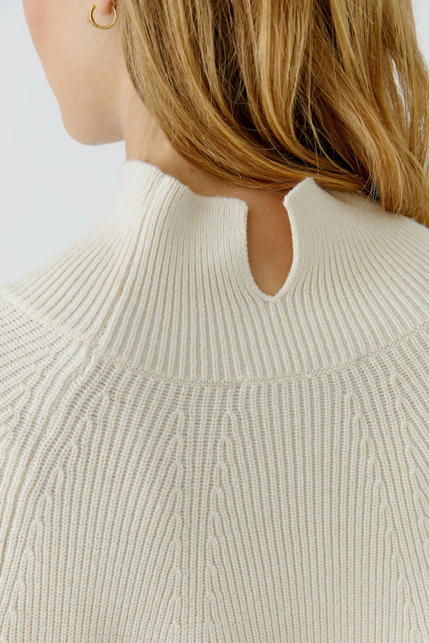 Woman in cream pullover with ribbed texture and keyhole back detail, showcasing casual style.