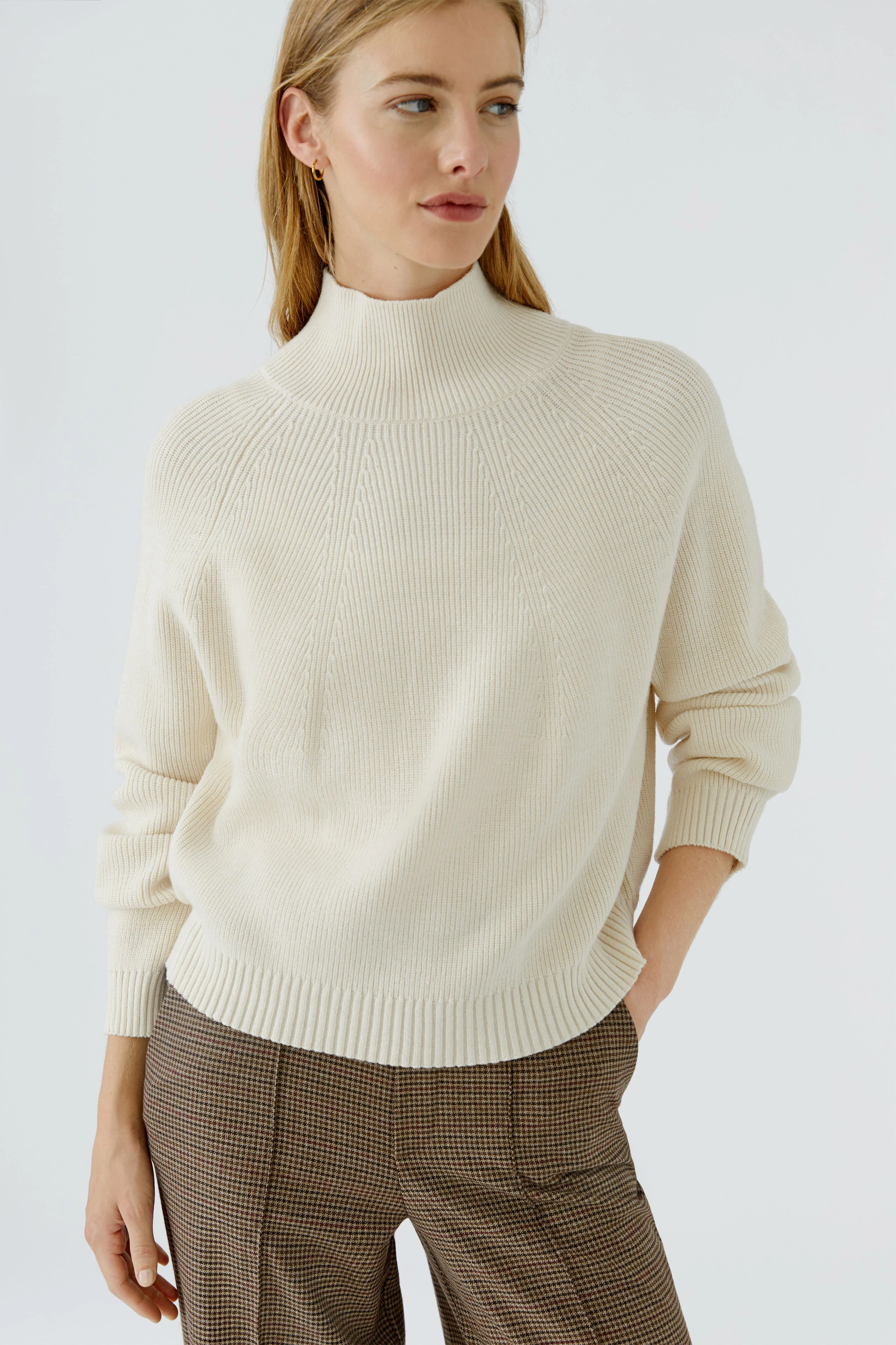 Damen-Pullover: Frau im cremefarbenen Pullover mit Stehkragen und karierter Hose, lässig und modern.