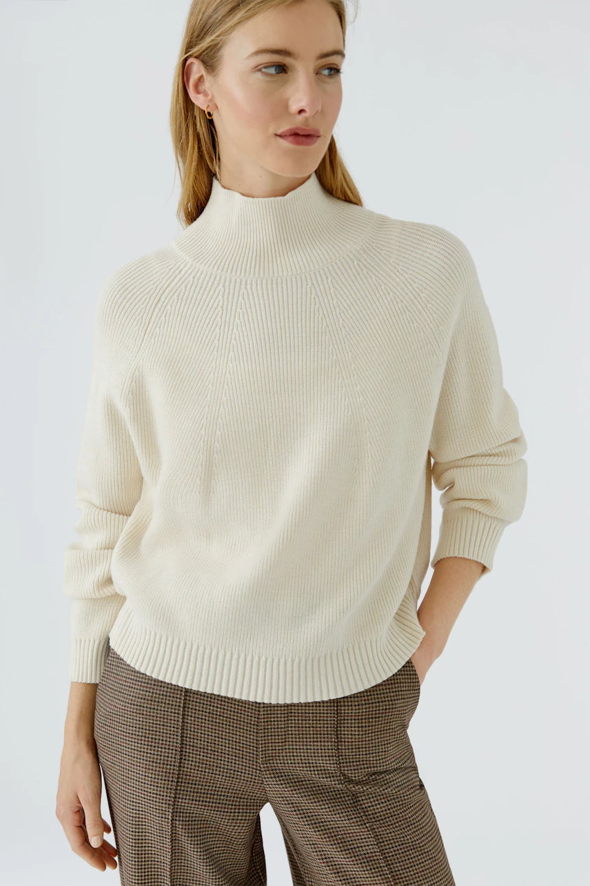 Casual women's pullover: Woman in cream pullover with ribbed texture and relaxed fit, paired with plaid pants.