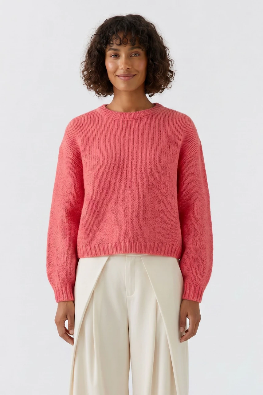 Frau im lässigen, korallfarbenen Pullover, kombiniert mit heller Hose, lächelt freundlich.