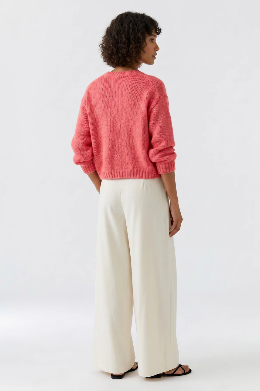 Frau im lässigen, rosa Pullover und weißen Hosen, von hinten gesehen.