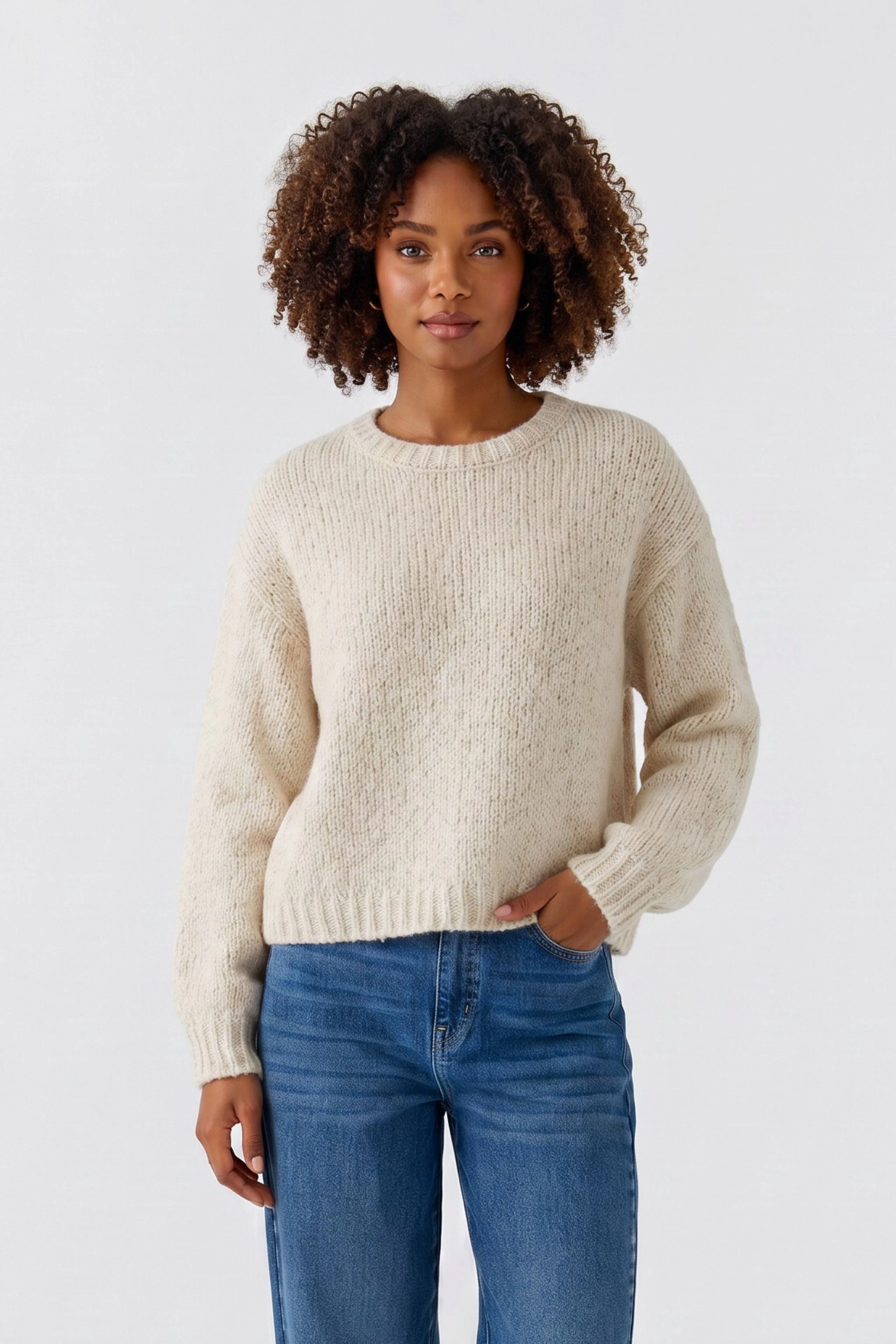 Lässiger Damen-Pullover: Frau im cremefarbenen Strickpullover und blauen Jeans, entspanntes Auftreten.