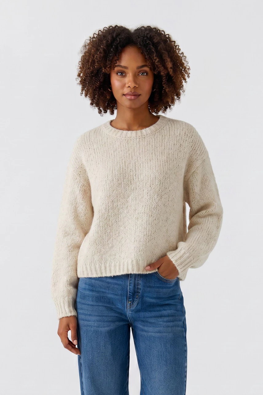 Lässiger Damen-Pullover: Frau im cremefarbenen Strickpullover und blauen Jeans, entspanntes Auftreten.
