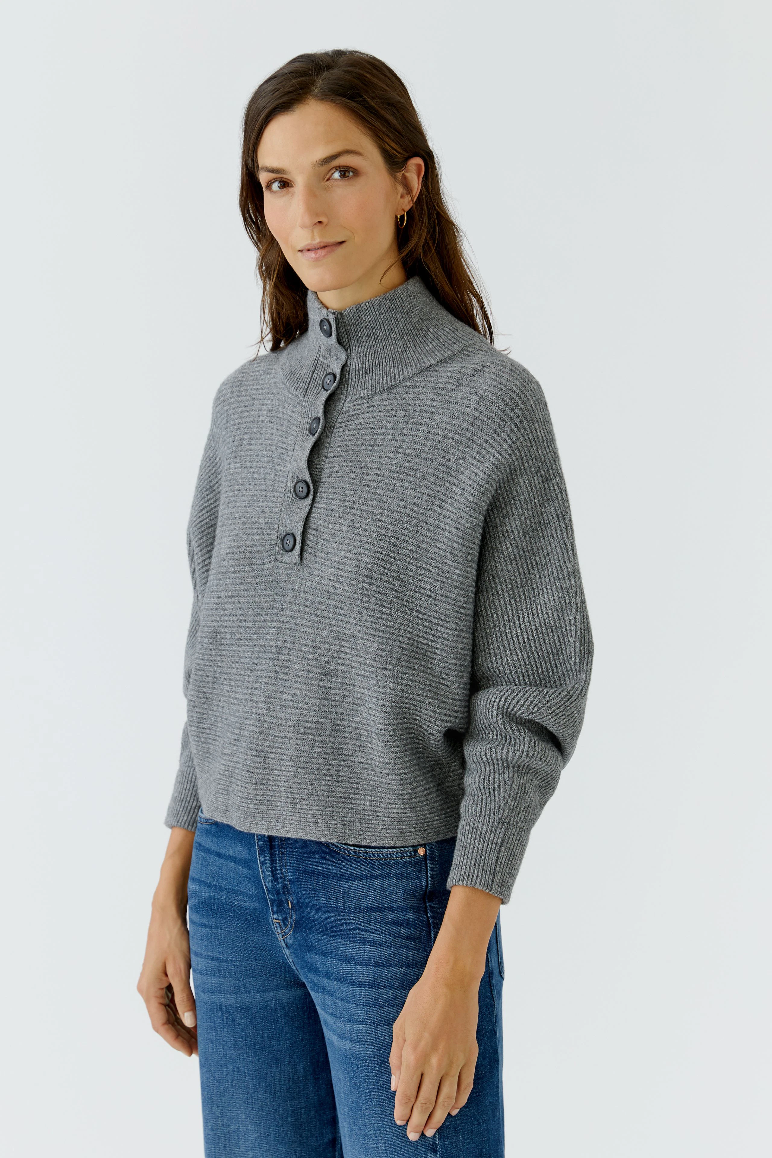 Grauer Damen-Pullover: Frau im lässigen Strickpullover mit Knopfleiste und blauen Jeans.
