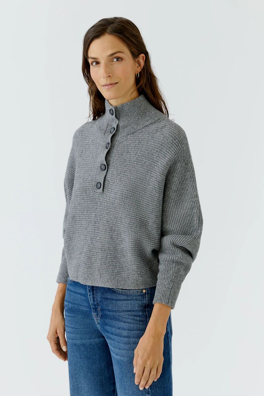 Grauer Damen-Pullover: Frau im lässigen Strickpullover mit Knopfleiste und blauen Jeans.