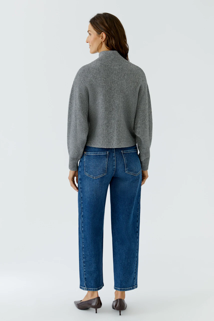 Grauer Damen-Pullover: Frau im lässigen Strickpullover und blauen Jeans, von hinten gesehen.