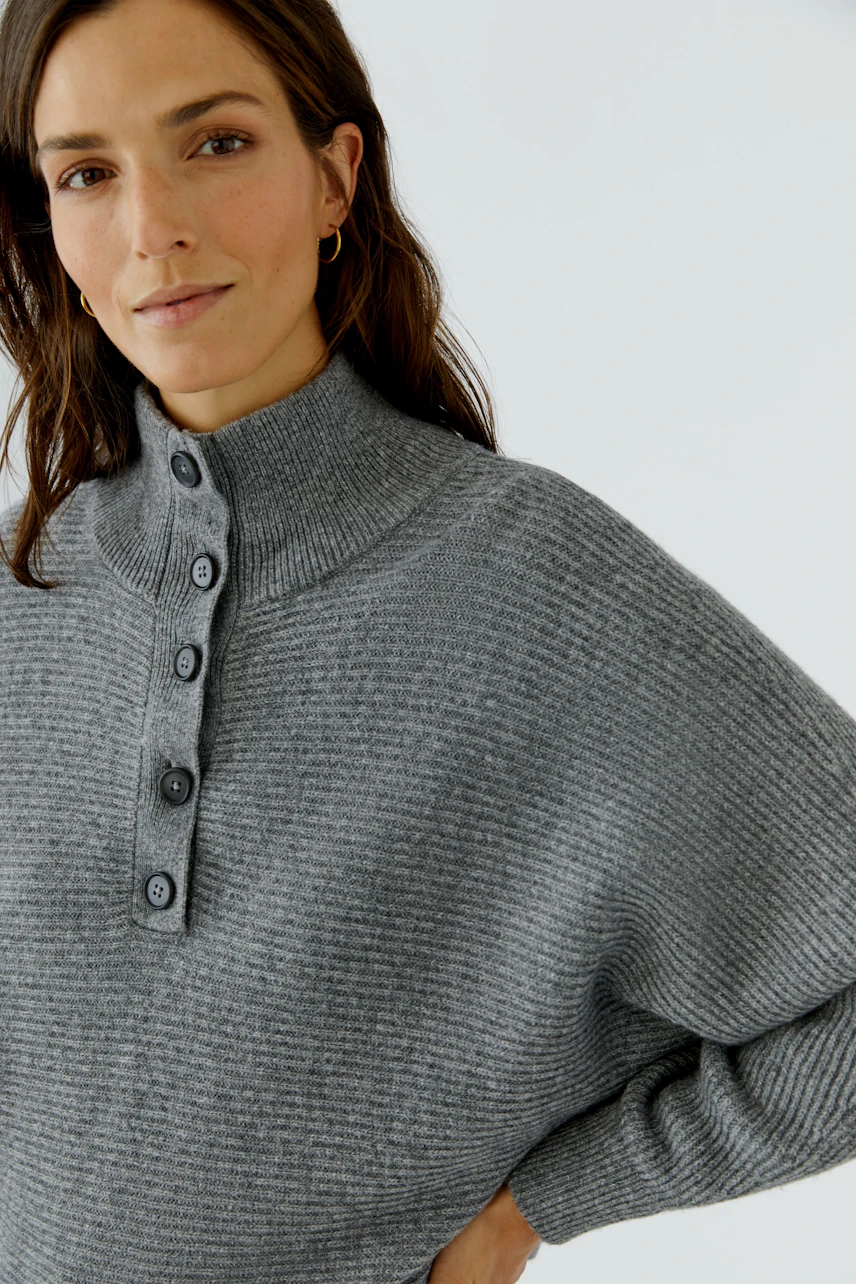 Grauer Damen-Pullover: Frau im lockeren Strickpullover mit Knopfleiste und Stehkragen, lässig und modern.
