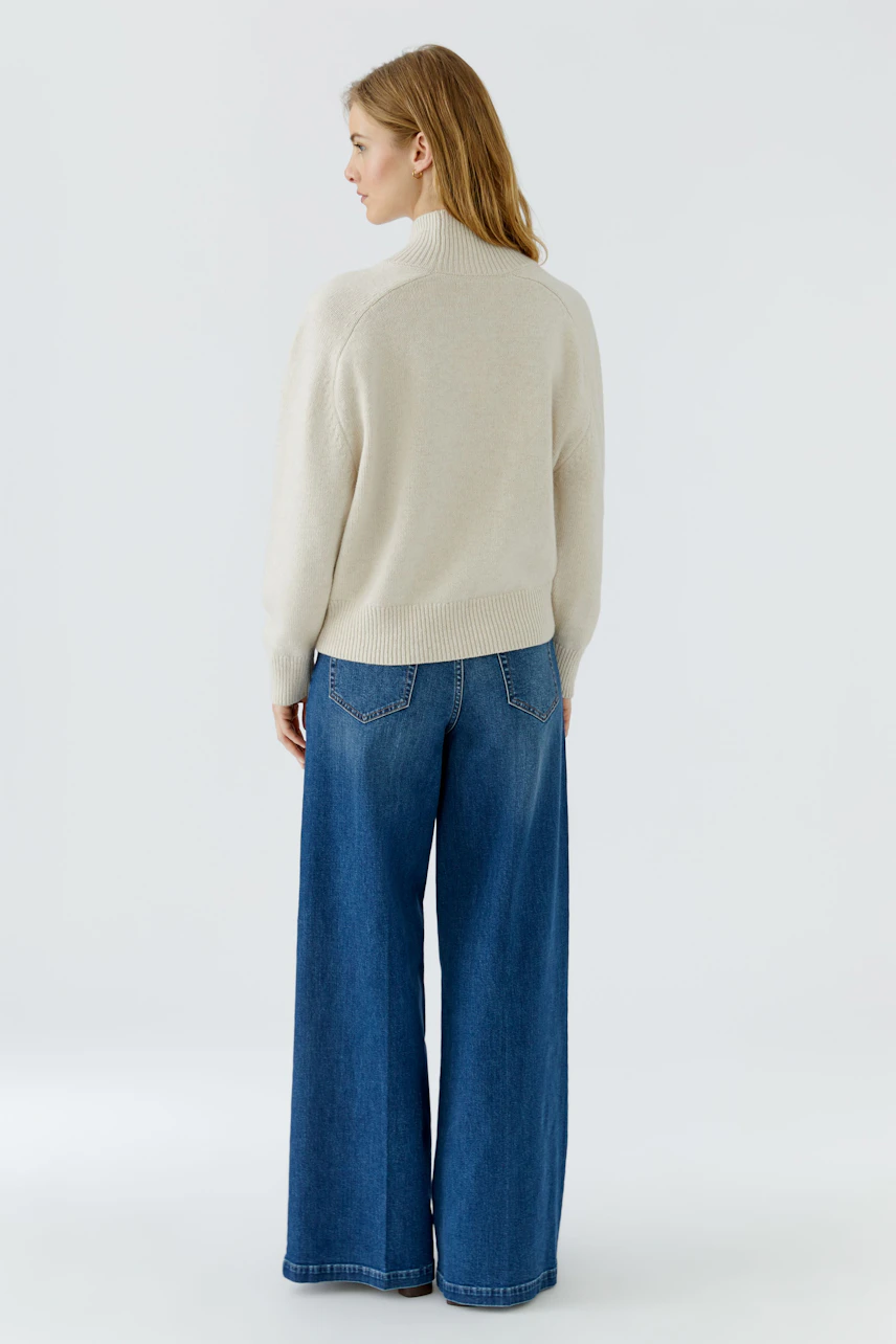 Damen-Pullover: Frau im cremefarbenen Pullover und blauer Jeans von hinten zu sehen.