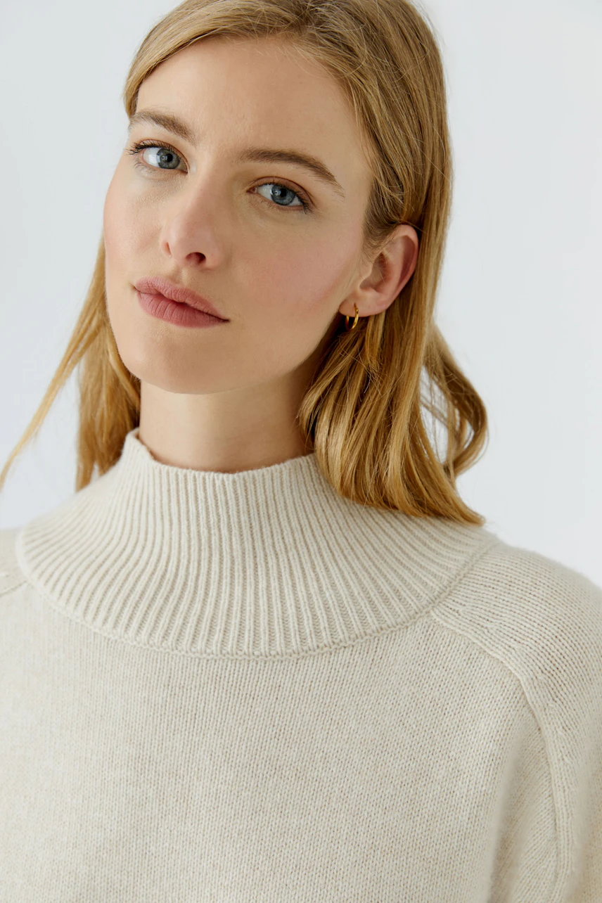 Damen-Pullover: Frau im cremefarbenen Pullover mit hohem Kragen, dezentes Design, weicher Stoff.