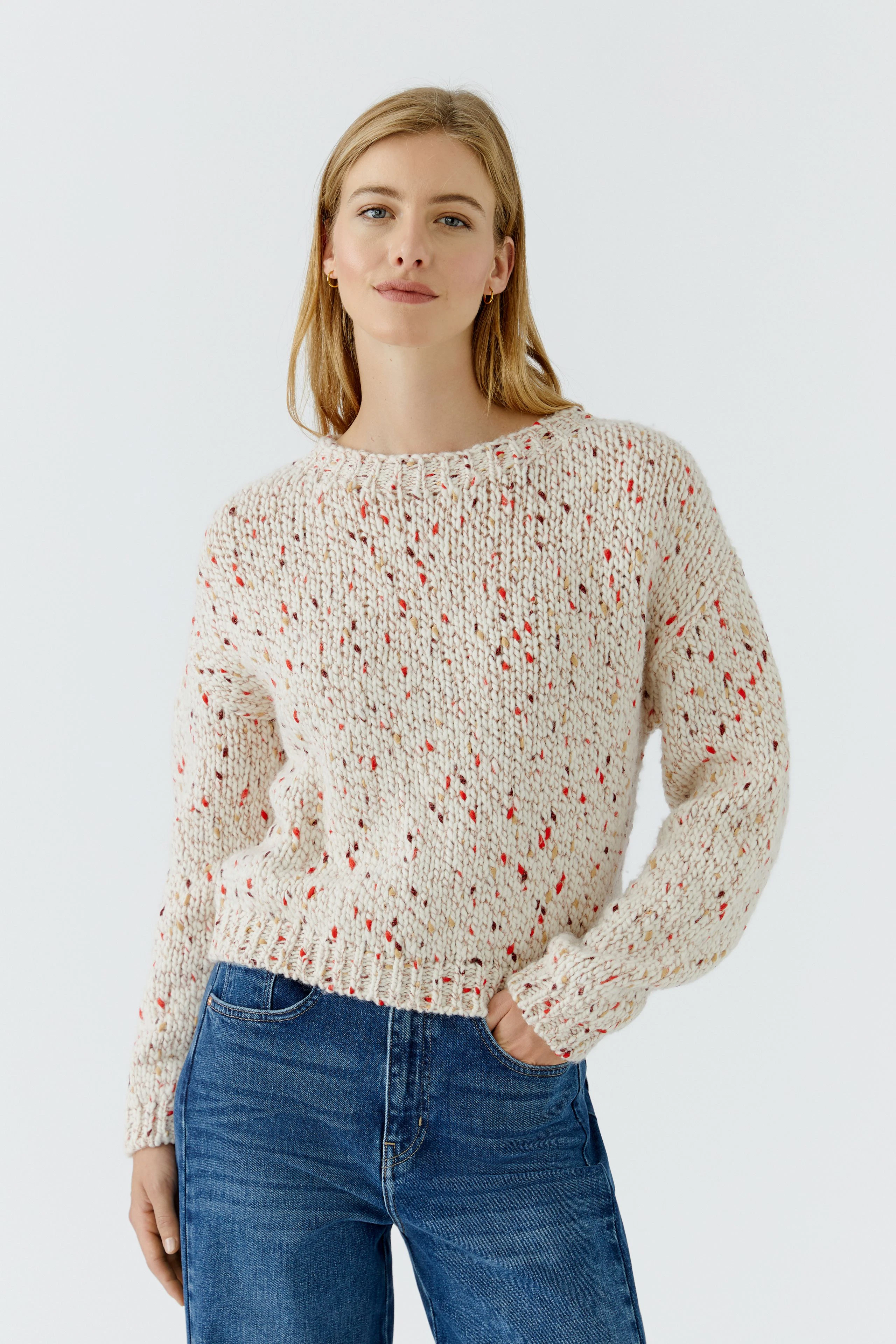 Lässiger Damen-Pullover: Frau im cremefarbenen Strickpullover mit roten Akzenten und blauen Jeans.