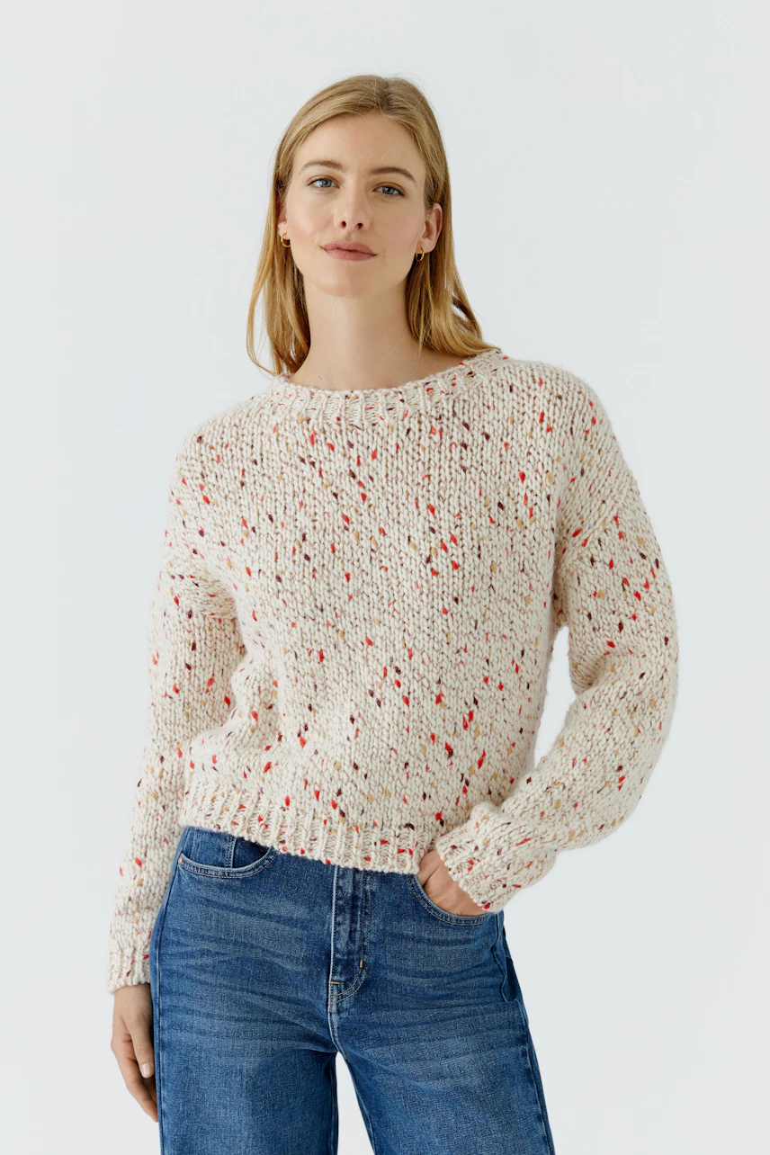 Lässiger Damen-Pullover: Frau im cremefarbenen Strickpullover mit roten Akzenten und blauen Jeans.