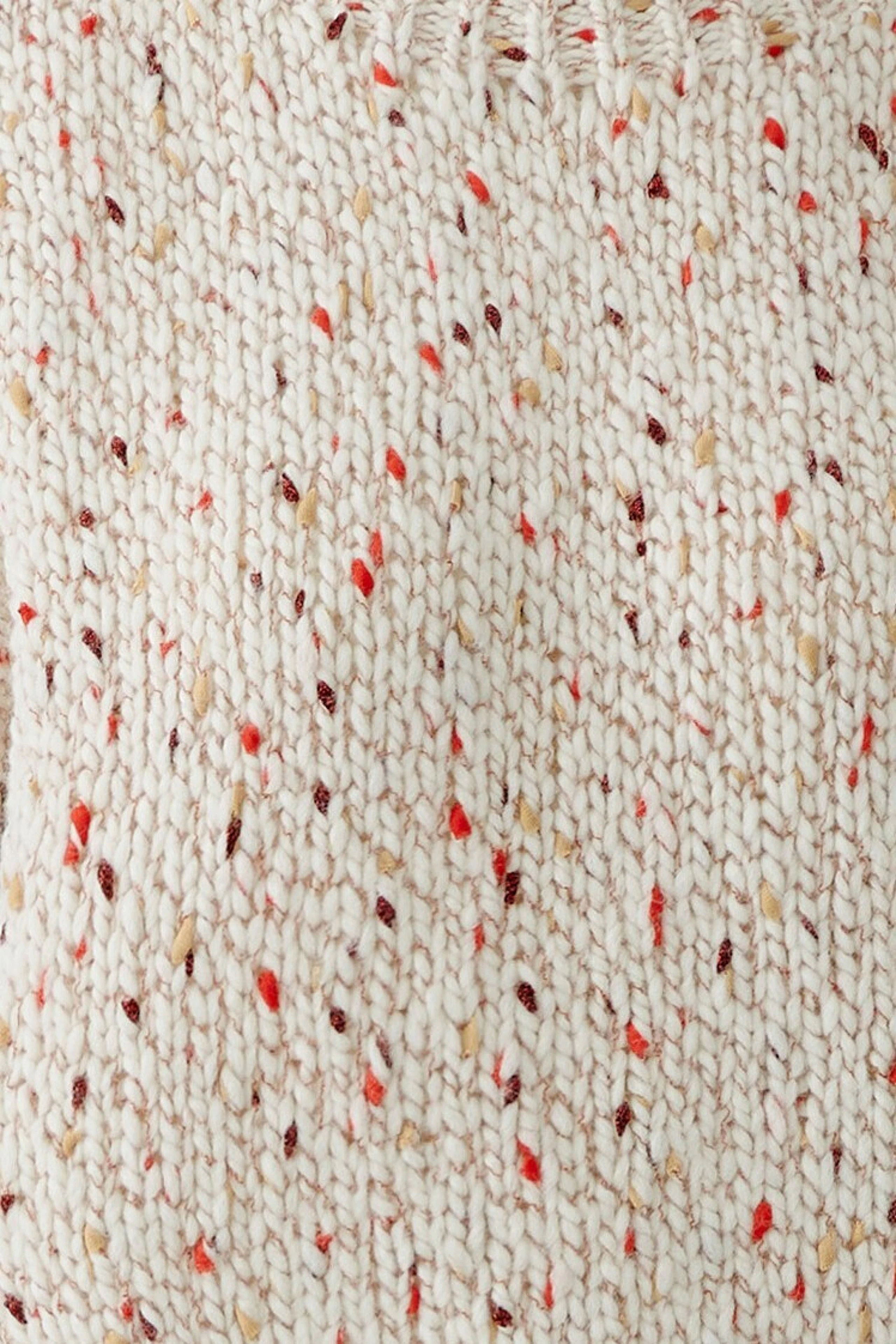 Frau im cremefarbenen Pullover mit roten Akzenten, lässig kombiniert mit blauer Jeans.