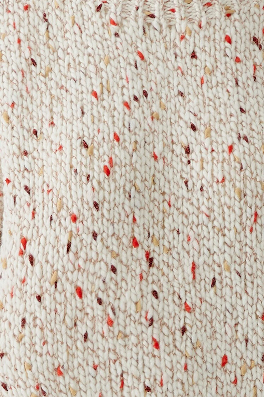 Frau im cremefarbenen Pullover mit roten Akzenten, lässig kombiniert mit blauer Jeans.