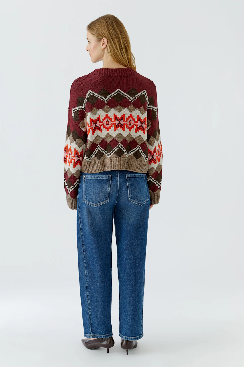 Frau im gemusterten Pullover: Bunter Strickpullover mit geometrischen Mustern, kombiniert mit blauen Jeans.