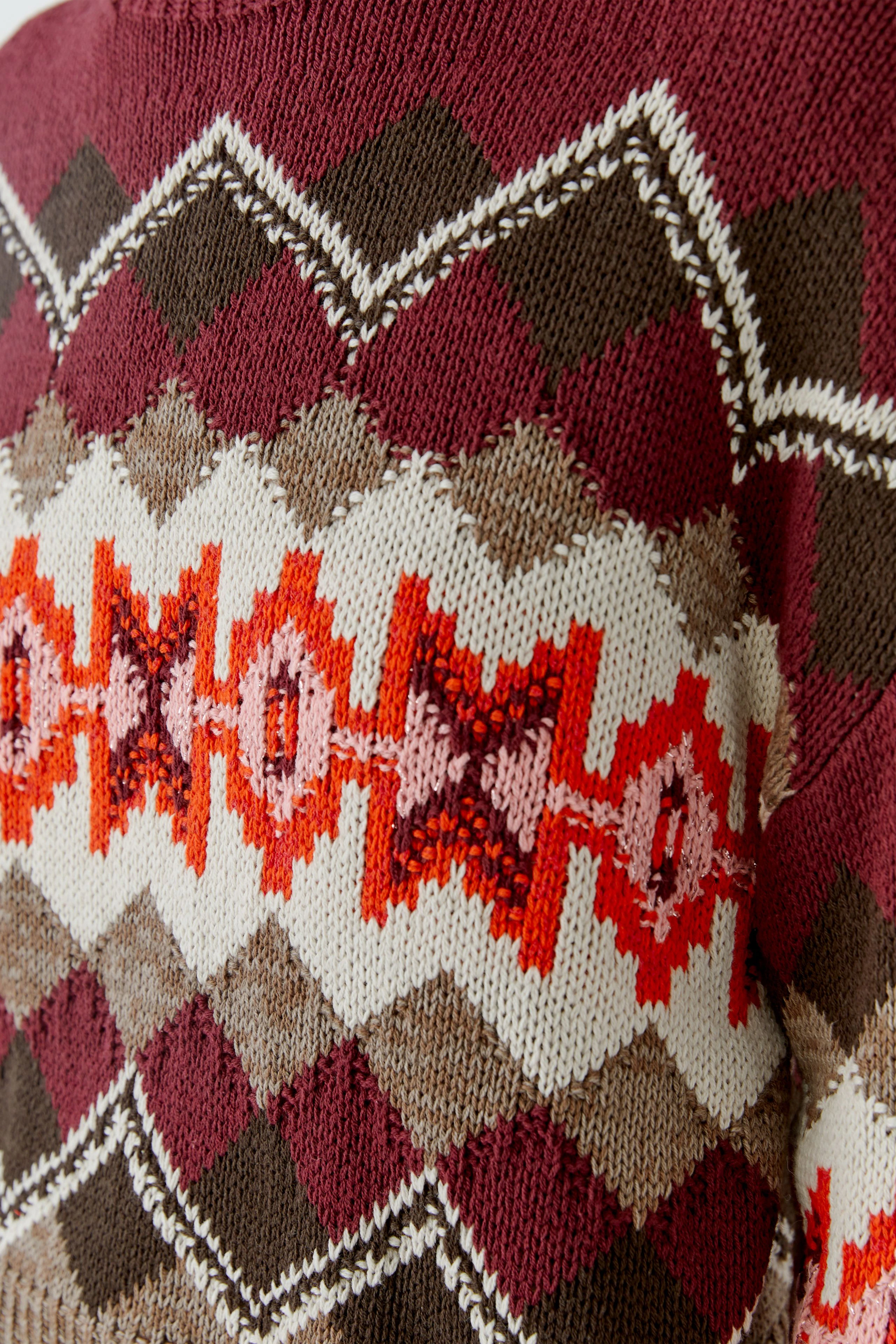 Bunter Damen-Pullover: Nahaufnahme eines Strickpullovers mit geometrischem Muster in Rot- und Brauntönen.