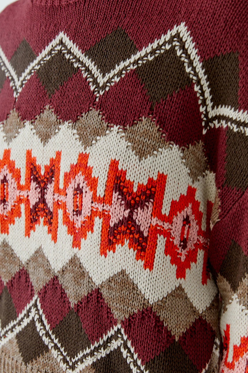 Bunter Damen-Pullover: Nahaufnahme eines Strickpullovers mit geometrischem Muster in Rot- und Brauntönen.