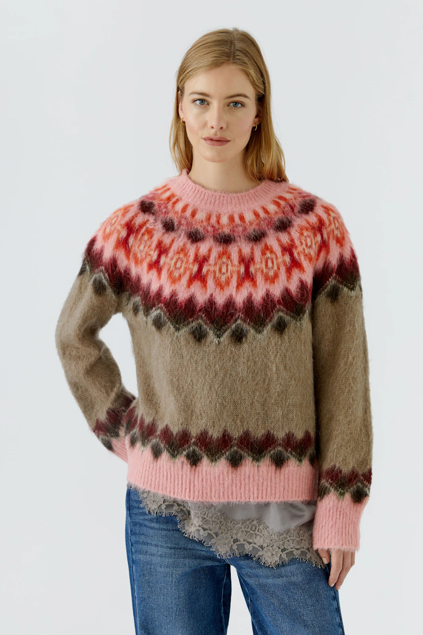 Frau im bunten Pullover mit Norwegermuster, kombiniert mit Jeans. Der Pullover ist flauschig und warm.