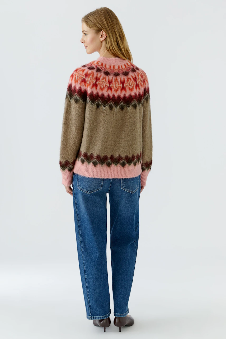Frau im bunten Pullover mit Norwegermuster, kombiniert mit blauen Jeans. Rückansicht des lässigen Outfits.