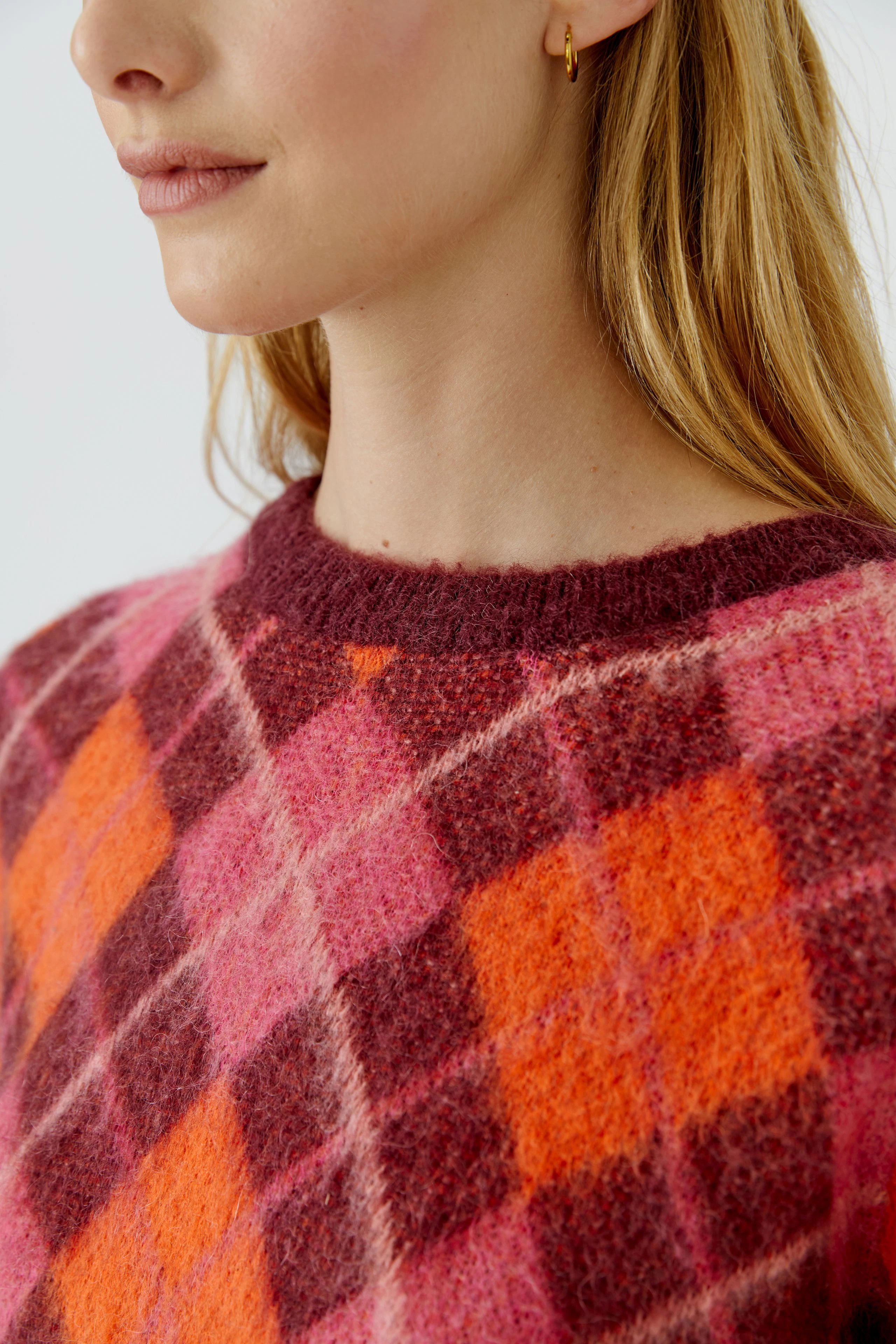 Frau im karierten Pullover in Rot- und Orangetönen, lässiger Look, ideal für kühle Tage.