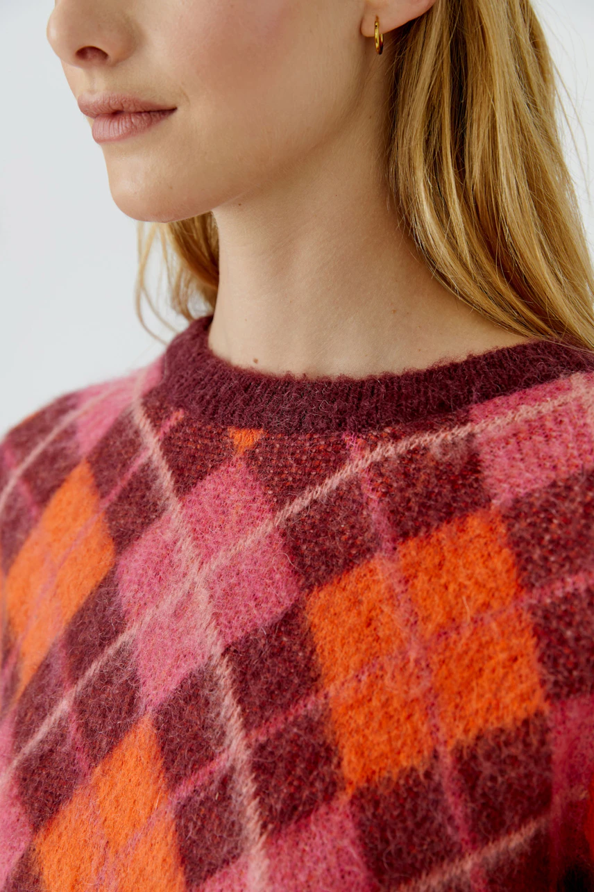 Frau im karierten Pullover in Rot- und Orangetönen, lässiger Look, ideal für kühle Tage.