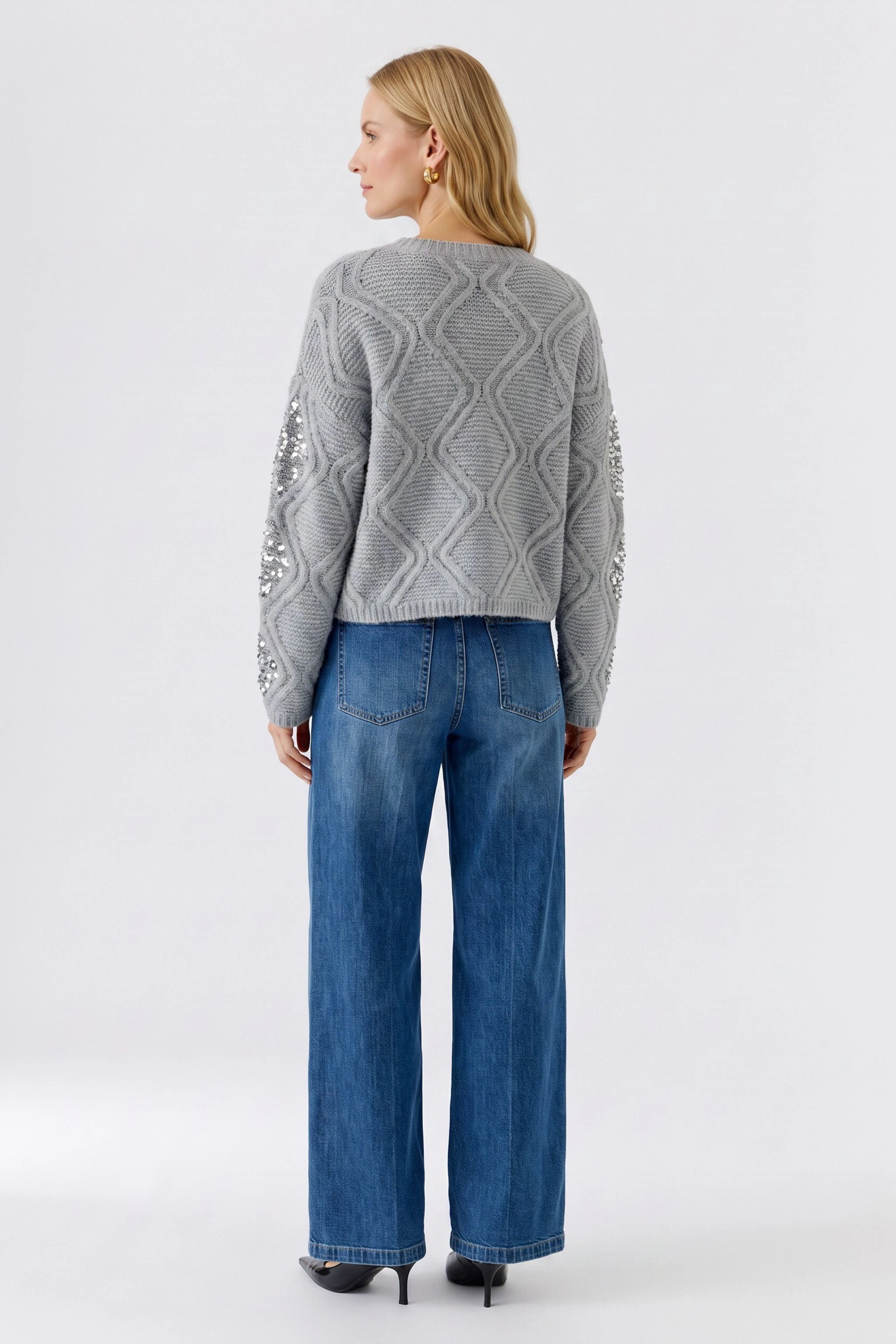 Grauer Damen-Pullover: Frau im strukturierten Pullover mit floralen Details, kombiniert mit blauen Jeans.