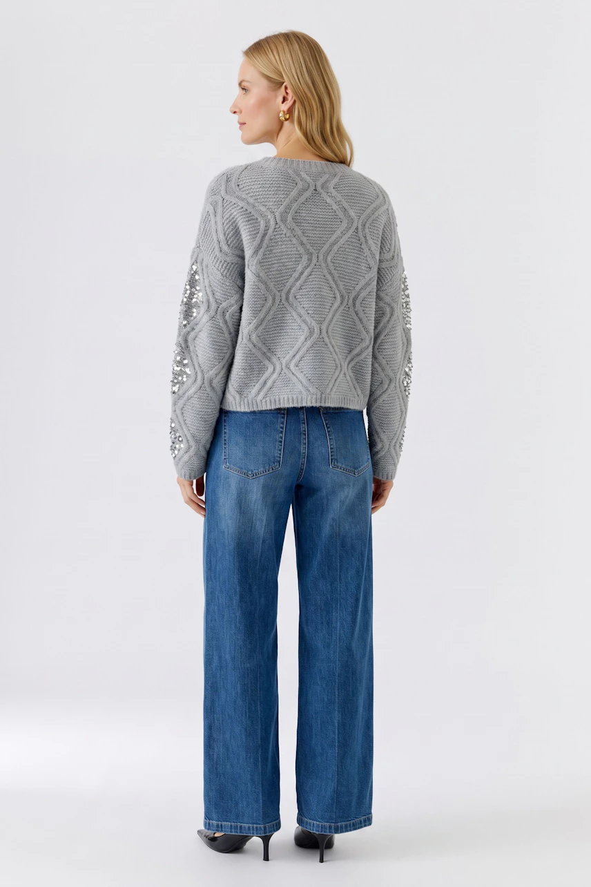 Grauer Damen-Pullover: Frau im strukturierten Pullover mit floralen Details, kombiniert mit blauen Jeans.