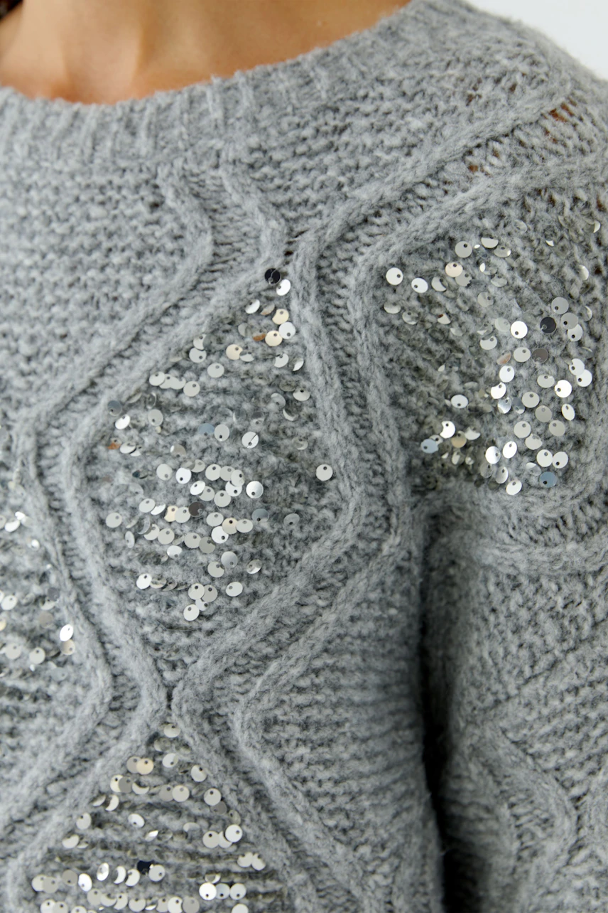 Grauer Damen-Pullover: Frau trägt gestrickten Pullover mit glänzenden Pailletten-Details.